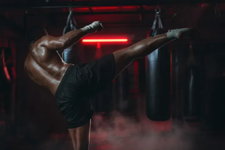 Coup de pied haut d'un kickboxeur, face aux sacs de frappe