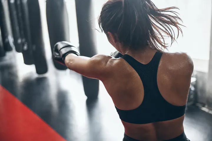 Une boxeuse frappe en gants, vue de dos, dans une salle claire